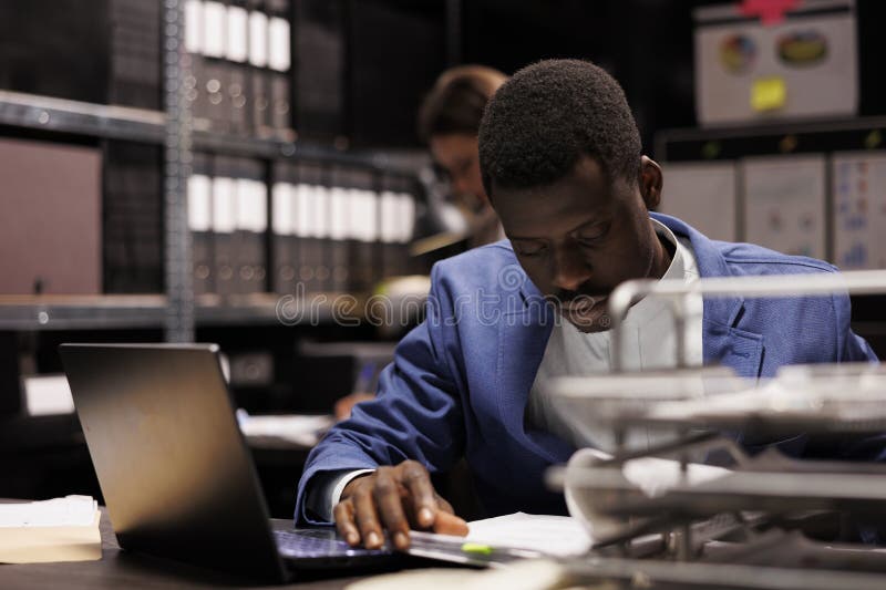 Businessman analyzing administrative files, searching for bureaucracy record in corporate depository. African american bookkeeper working late at night at accountancy report. Businessman analyzing administrative files, searching for bureaucracy record in corporate depository. African american bookkeeper working late at night at accountancy report