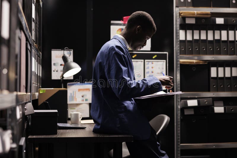 Businessman reading administrative files, analyzing bureaucracy report working overtime in storage room. African american manager checking accountancy record in corporate depository. Businessman reading administrative files, analyzing bureaucracy report working overtime in storage room. African american manager checking accountancy record in corporate depository