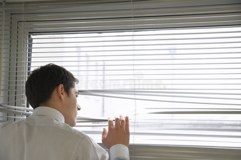 Geschäftsmann Looking Through Blinds stockbild