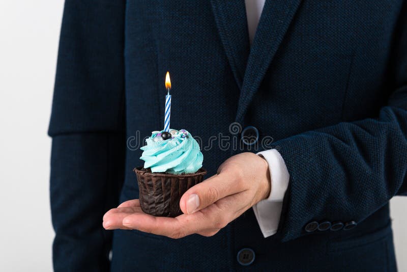 Businessman holding birthday cupcake with birning candle. Business greeting card. 1 year. Corporate party. Copy space for text. Businessman holding birthday cupcake with birning candle. Business greeting card. 1 year. Corporate party. Copy space for text