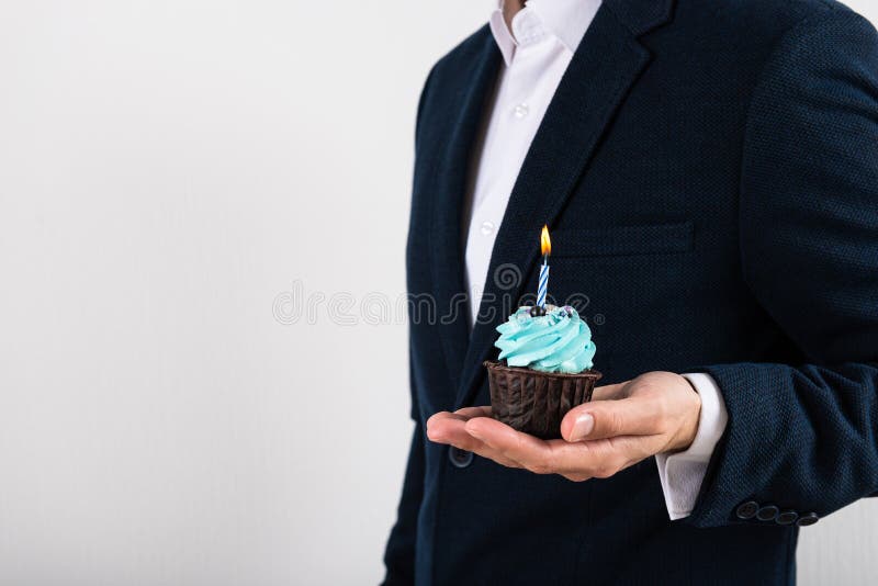 Businessman holding birthday cupcake with birning candle. Business greeting card. 1 year. Corporate party. Copy space for text. Businessman holding birthday cupcake with birning candle. Business greeting card. 1 year. Corporate party. Copy space for text