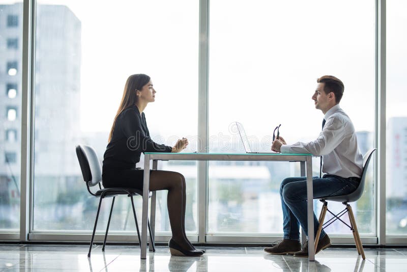 Geschäftsmann und Frau, die eine Diskussion im Büro vertraulich bei Tisch gegen Fenster hat stockbild Geschäftsmann und Frau, die eine Diskussion im Büro vertraulich bei Tisch gegen Fenster hat stockbild
