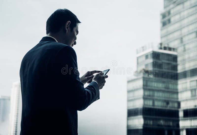 Geschäftsmann unter Verwendung des Handys nahe Bürofenster an Büro buil lizenzfreies stockfoto Geschäftsmann unter Verwendung des Handys nahe Bürofenster an Büro buil lizenzfreies stockfoto
