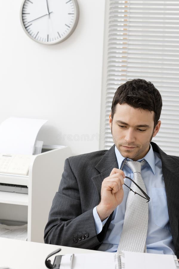 Portrait of young businessman thinking, holding his glasses, looking down. Portrait of young businessman thinking, holding his glasses, looking down.