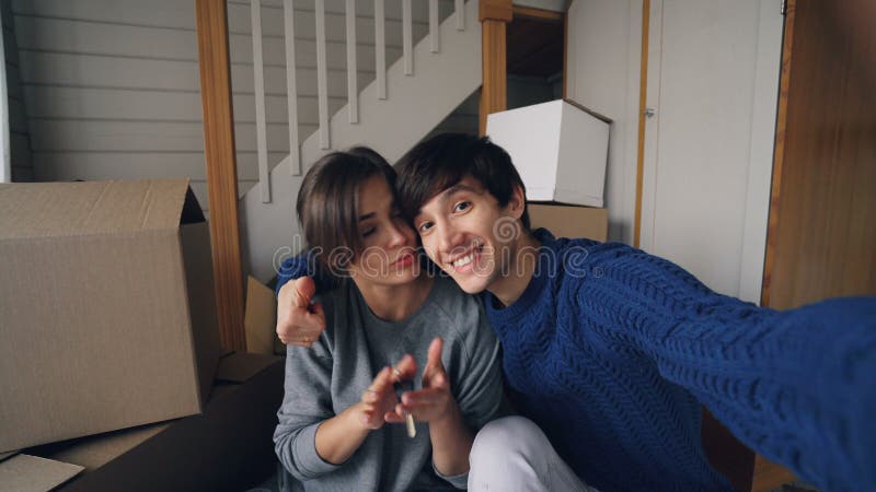 Gesichtspunkt geschossen vom schönen Mann, der selfie mit seiner hübschen Frau im neuen Haus Schlüssel küssend, umarmend und zeig
