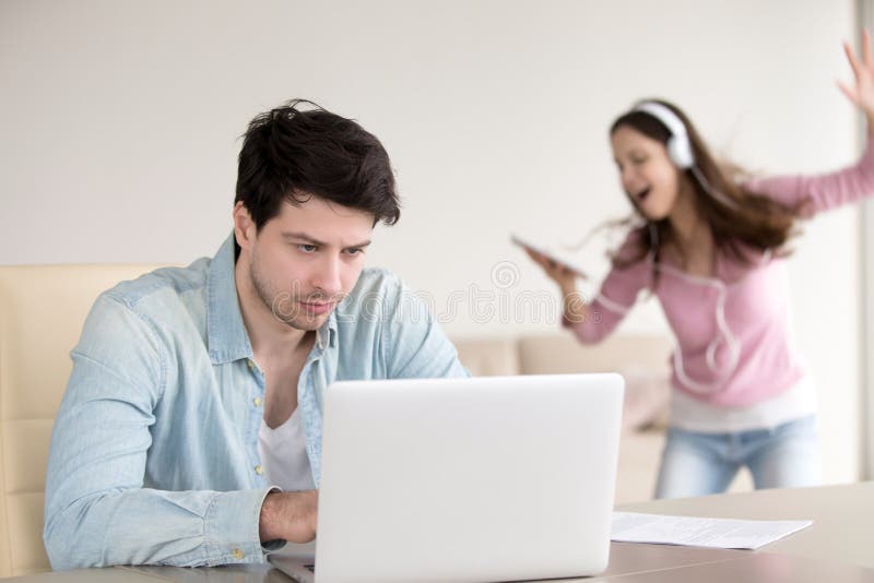 Gestörter Mann, der an Laptop, Frauentanzen in Kopfhörer indoo arbeitet lizenzfreies stockbild Gestörter Mann, der an Laptop, Frauentanzen in Kopfhörer indoo arbeitet lizenzfreies stockbild