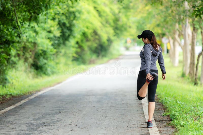 Gesunde lächelnde Frau wärmen sich auf und streckt sich die Arme aus und blickt auf die Straße im Freien Asiatische Läuferin trai