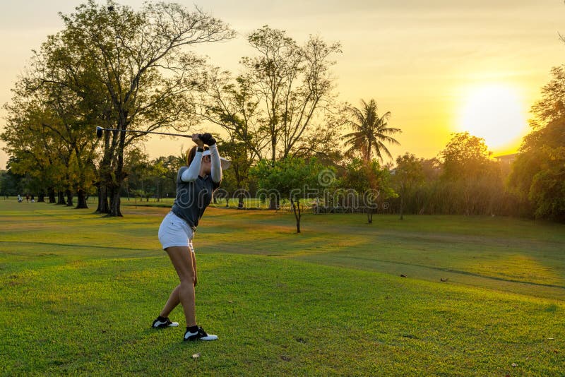 Gesunder Sport Asiatische Sportlerin Golfer-Spieler, die Golf-Swing-Abschlag auf den grünen Golfplatz abends, sie wahrscheinlich