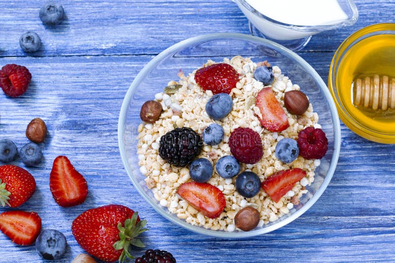 Gesundes muesli mit Himbeere, Blaubeere, Erdbeere, Blackberry, Haselnuss, Milch und Honig auf blauer hölzerner rustikaler Tabelle lizenzfreie stockfotos Gesundes muesli mit Himbeere, Blaubeere, Erdbeere, Blackberry, Haselnuss, Milch und Honig auf blauer hölzerner rustikaler Tabelle lizenzfreie stockfotos