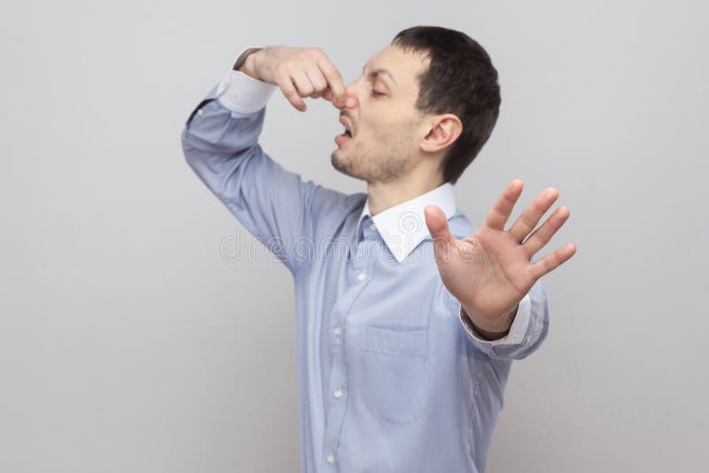 Get out from here. Portrait of handsome bristle businessman in classic light blue shirt standing holding his nose and showing stop stock image Get out from here. Portrait of handsome bristle businessman in classic light blue shirt standing holding his nose and showing stop stock image