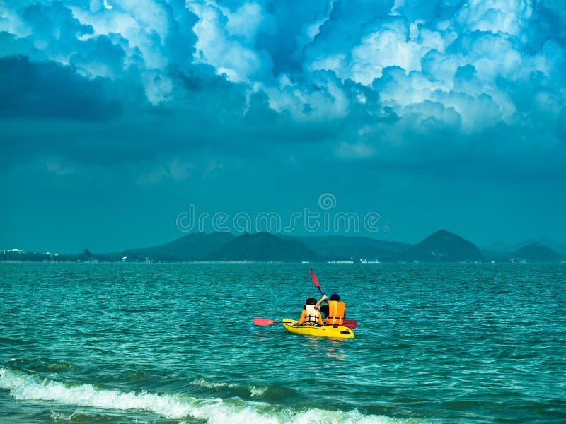 Getontes Bild eines gelben Kajaks mit zwei Touristen segelt auf das Meer auf dem Hintergrund des drastischen Himmels lizenzfreies stockfoto Getontes Bild eines gelben Kajaks mit zwei Touristen segelt auf das Meer auf dem Hintergrund des drastischen Himmels lizenzfreies stockfoto