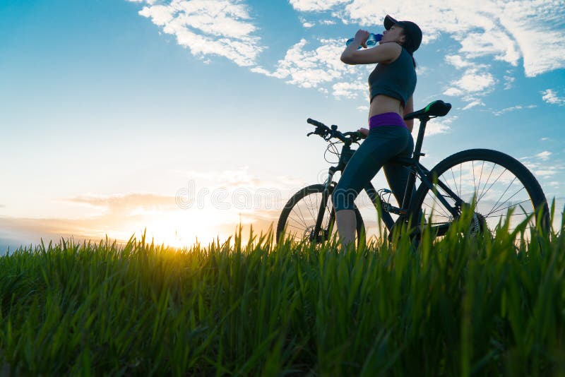 Getr?nkwasser w?hrend der Trainings sport Frau auf Fahrradsonnenuntergang stockbilder Getr?nkwasser w?hrend der Trainings sport Frau auf Fahrradsonnenuntergang stockbilder