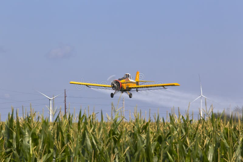 A agricultural plane dusts crops against a blue sky. A agricultural plane dusts crops against a blue sky