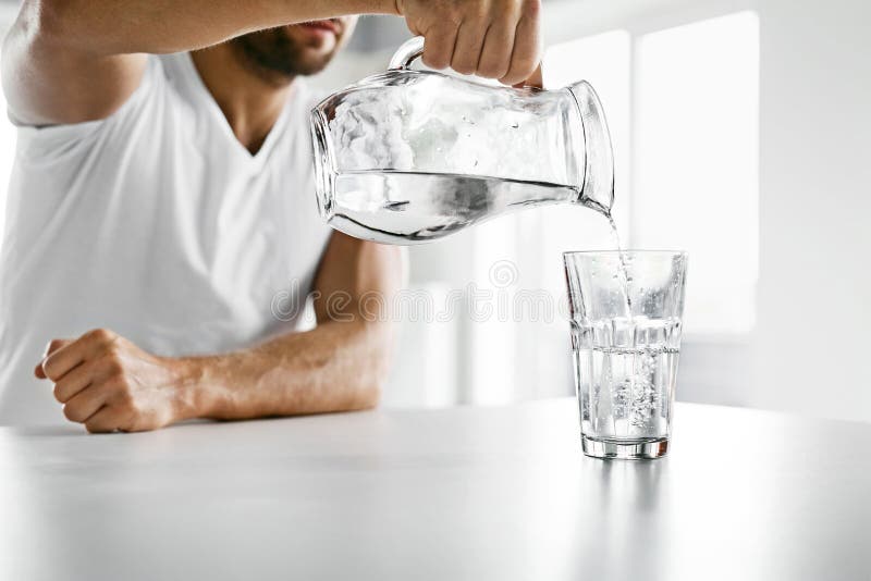 Drink Water. Close Up Of Handsome Young Man Pouring Fresh Pure Water From Pitcher Into A Glass In Morning In Kitchen. Beautiful Athletic Male Model Feeling Thirsty. Healthy Nutrition And Hydration. Drink Water. Close Up Of Handsome Young Man Pouring Fresh Pure Water From Pitcher Into A Glass In Morning In Kitchen. Beautiful Athletic Male Model Feeling Thirsty. Healthy Nutrition And Hydration