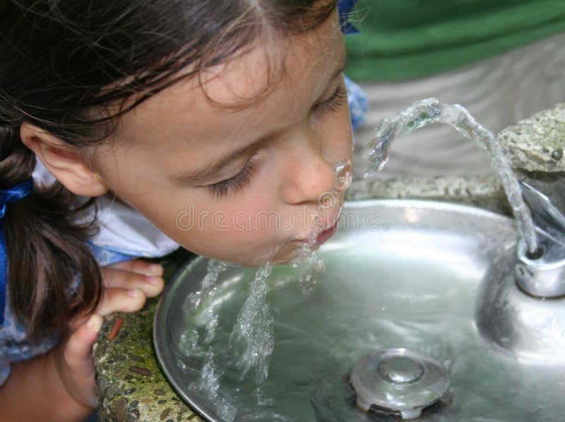 Graziosa ragazza che beve da una fontana di acqua.