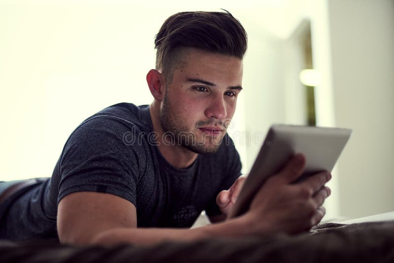 Getting to know his new gadget. a young man using his wireless tablet while lying on his bed at home. royalty free stock photography