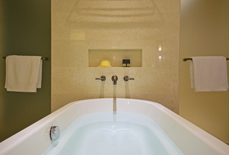 Gevulde witte badkuip met messingskraan opgezet op de marmeren muur en doucheschermen aan beide kanten
