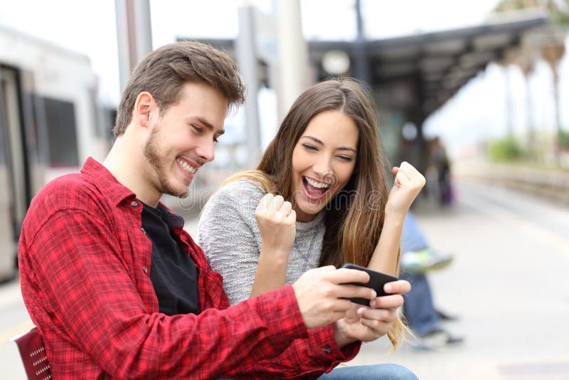 Gewinnende Online-Spiele des glücklichen Paars in einer Bahnstation stockfoto Gewinnende Online-Spiele des glücklichen Paars in einer Bahnstation stockfoto