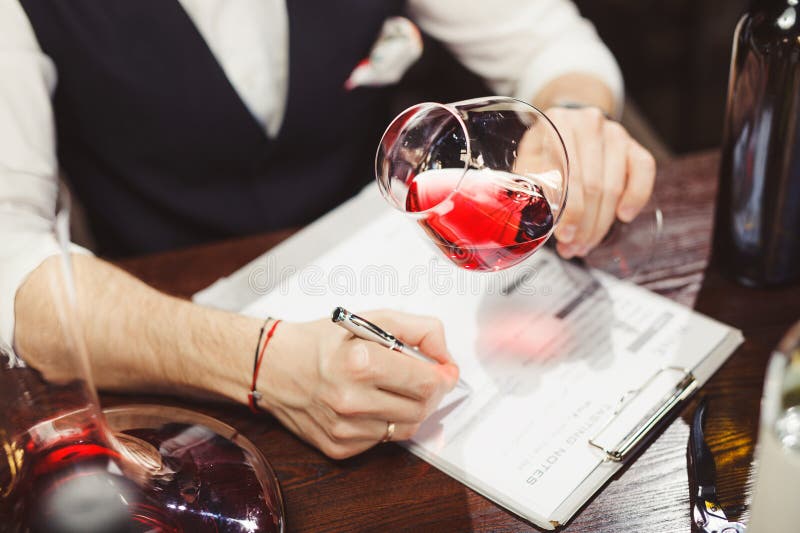 Faceless man evaluates alcoholic drink, describes it with rating on paper. Wine expert writes report, information on beverage, tasting notes on table with bottles, wineglasses, corkscrew. Faceless man evaluates alcoholic drink, describes it with rating on paper. Wine expert writes report, information on beverage, tasting notes on table with bottles, wineglasses, corkscrew.