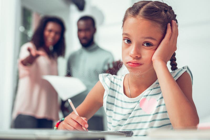 Gezichtsportret van meisje die lessen doen wanneer haar ouders het spreken royalty-vrije stock afbeeldingen Gezichtsportret van meisje die lessen doen wanneer haar ouders het spreken royalty-vrije stock afbeeldingen