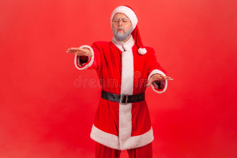 Vision problems. Portrait of blind disoriented lonely elderly man in santa claus costume walking with closed eyes, raising hands to search lost road. Indoor studio shot isolated on red background. Vision problems. Portrait of blind disoriented lonely elderly man in santa claus costume walking with closed eyes, raising hands to search lost road. Indoor studio shot isolated on red background.