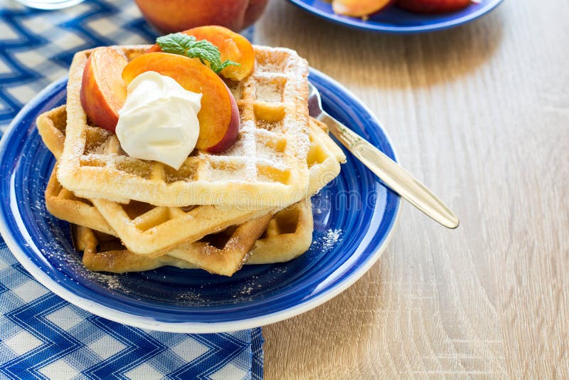 Gezond ontbijt: Belgische wafels met perzikplakken en room verfraaide muntbladeren en blauw servet royalty-vrije stock afbeelding Gezond ontbijt: Belgische wafels met perzikplakken en room verfraaide muntbladeren en blauw servet royalty-vrije stock afbeelding