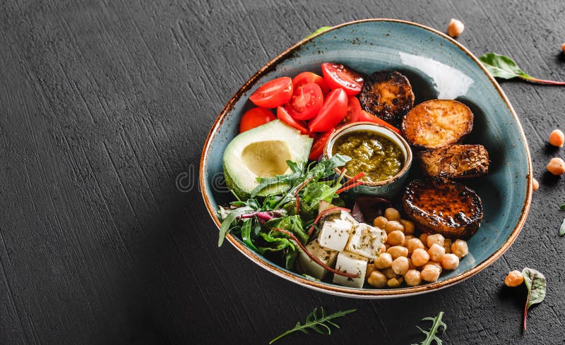 Gezonde de komschotel van Boedha met avocado, tomaat, kaas, kikkererwt, verse arugulasalade, aardappelen in de schil en sauspesto royalty-vrije stock fotografie Gezonde de komschotel van Boedha met avocado, tomaat, kaas, kikkererwt, verse arugulasalade, aardappelen in de schil en sauspesto royalty-vrije stock fotografie