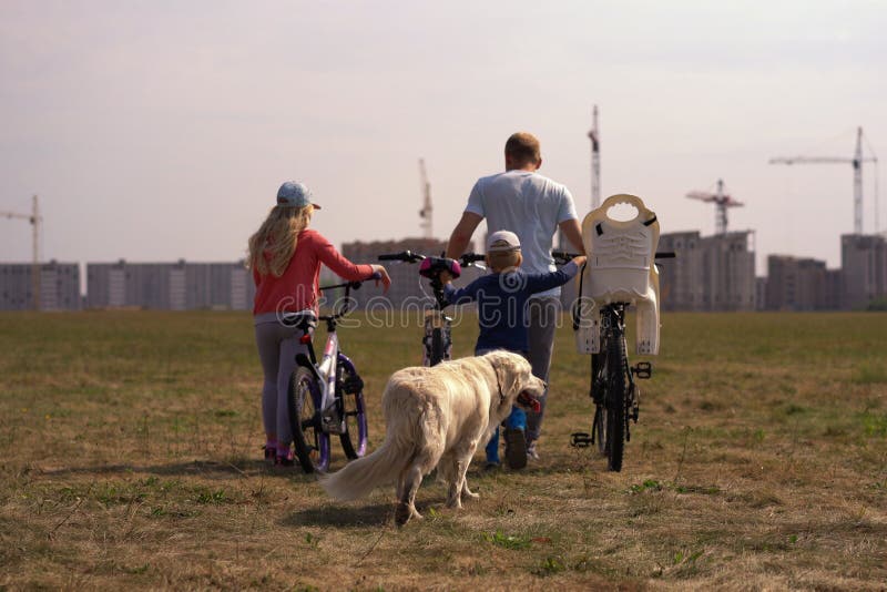 Gezonde levensstijl - familie met fietsen en een hond die langs het gebied dichtbij de stad lopen stock foto's Gezonde levensstijl - familie met fietsen en een hond die langs het gebied dichtbij de stad lopen stock foto's