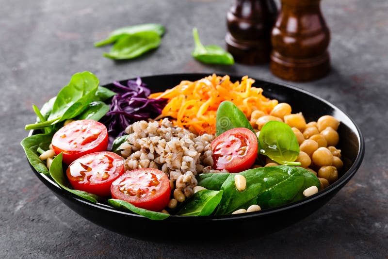 Gezonde vegetarische schotel met boekweit en plantaardige salade van kikkererwt, boerenkool, wortel, verse tomaten, spinazieblade