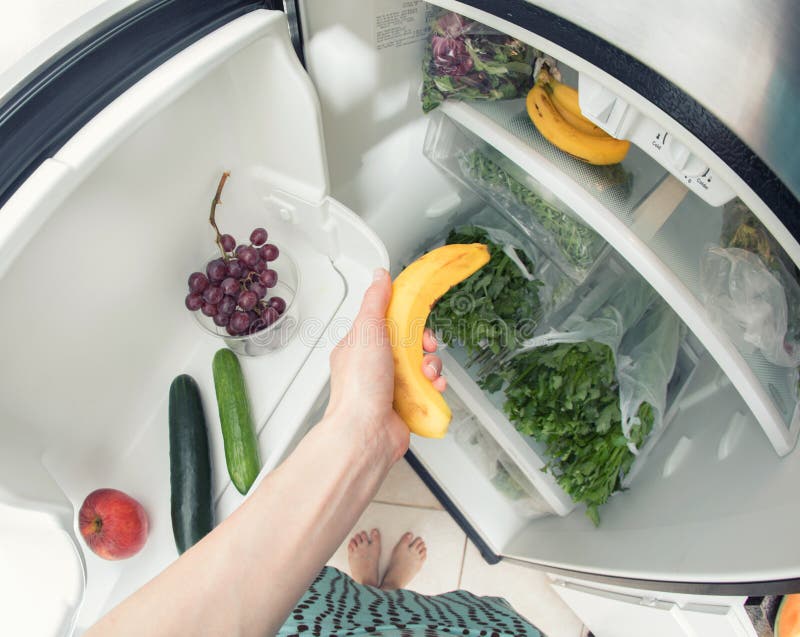 Gezonde voeding: Een hand die een banaan van het open ijskasthoogtepunt grijpen van greens stock fotografie Gezonde voeding: Een hand die een banaan van het open ijskasthoogtepunt grijpen van greens stock fotografie