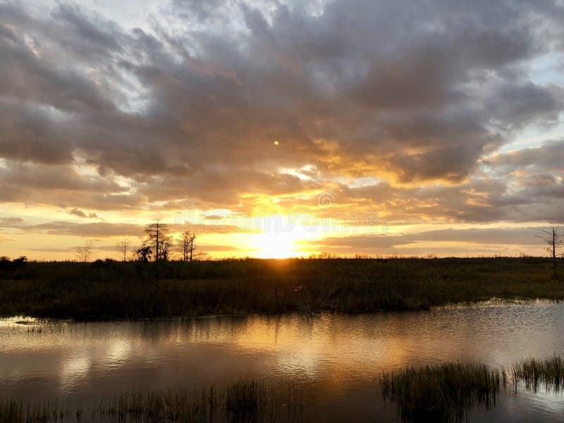 Sunset in the swamps. Giant orange sun sets behind the bayou of a cypress swamp and reflects in the river stock photo Sunset in the swamps. Giant orange sun sets behind the bayou of a cypress swamp and reflects in the river stock photo