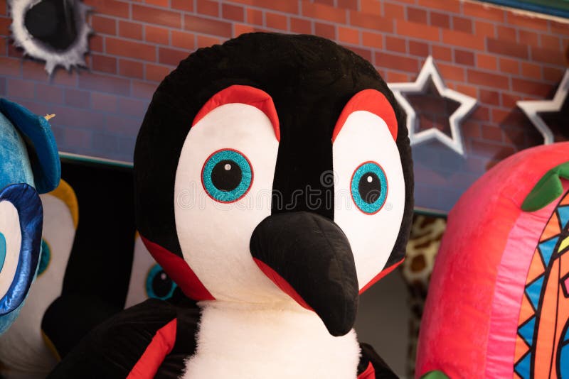 Giant penguin plush toy hanging on a wall among other tyos at outdoors market fair. Giant penguin plush toy hanging on a wall among other tyos at outdoors market fair.