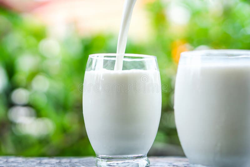 Gietende melk bij het drinken van glas over de ochtendachtergrond van het aardzonlicht royalty-vrije stock foto's Gietende melk bij het drinken van glas over de ochtendachtergrond van het aardzonlicht royalty-vrije stock foto's