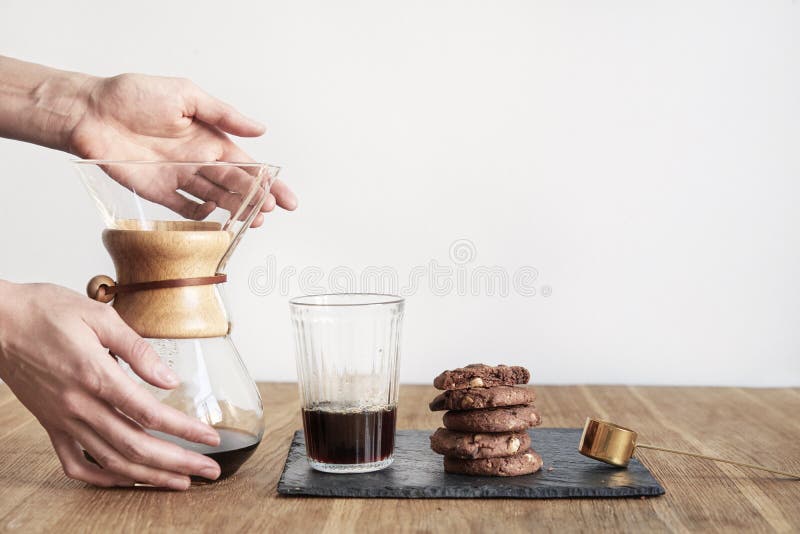Gießen Sie über Kaffeebrauverfahren Chemex, Frauenhandgriff eine Glasschüssel, Stillleben mit Schokoladenkuchenplätzchen auf Holz lizenzfreie stockfotografie Gießen Sie über Kaffeebrauverfahren Chemex, Frauenhandgriff eine Glasschüssel, Stillleben mit Schokoladenkuchenplätzchen auf Holz lizenzfreie stockfotografie