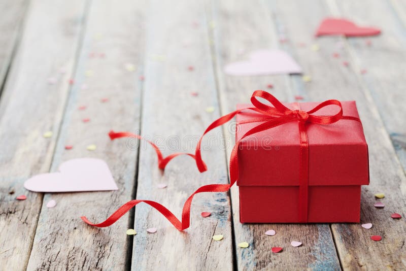 Gift box with red bow ribbon and paper heart on table for Valentines day