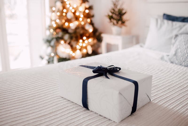Gift box on a white bed close up. Christmas tree and window with the morning light at background
