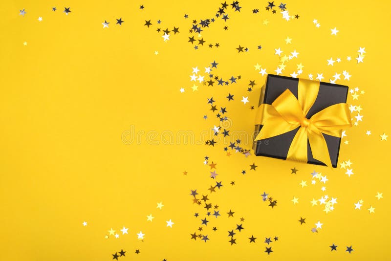 Gift box on yellow background with sparkling confetti