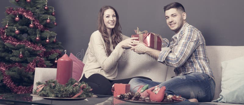 Young couple while gift giving at christmas sitting on the sofa at home. Young couple while gift giving at christmas sitting on the sofa at home