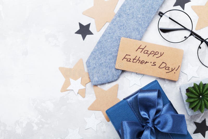 Gift or present box, paper tag with Happy Fathers Day, eyeglasses and necktie on white table top view. Flat lay composition.