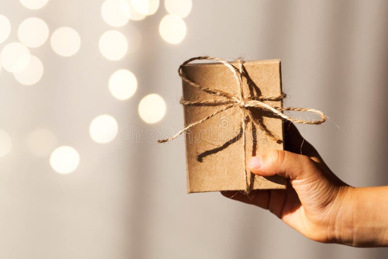 A gift with your own hands. Craft gift box in hand on the background of Christmas lights. Copy space