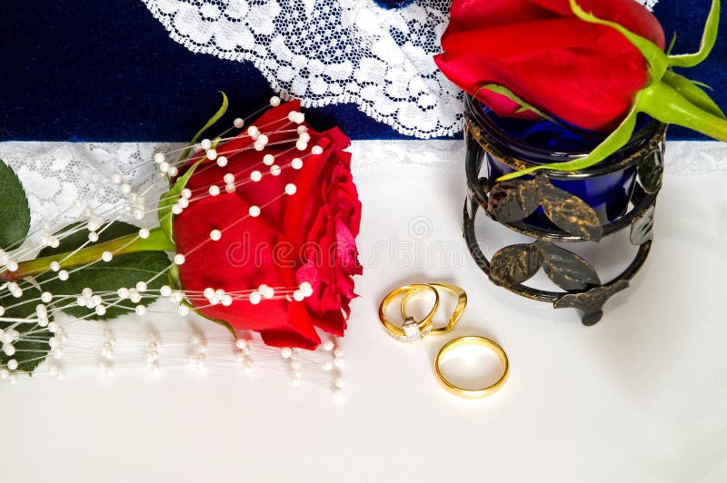 Beautiful engagement and wedding rings and red rose sit in front of a lacy, blue wedding photo album. Valentines Special!. Beautiful engagement and wedding rings and red rose sit in front of a lacy, blue wedding photo album. Valentines Special!