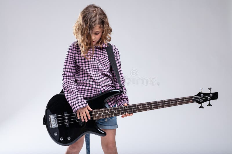 Gifted young girl progeny playing an electric guitar with downcast head absorbed in the music over a grey studio background. Gifted young girl progeny playing an electric guitar with downcast head absorbed in the music over a grey studio background