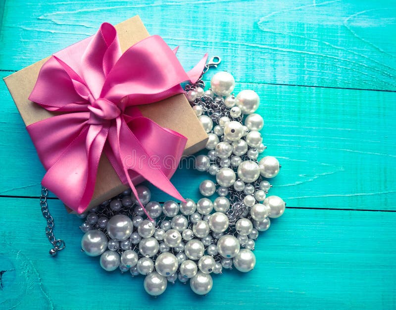Giftvakje met roze lintboog en pareljuwelen op blauwe houten lijst stock foto Giftvakje met roze lintboog en pareljuwelen op blauwe houten lijst stock foto