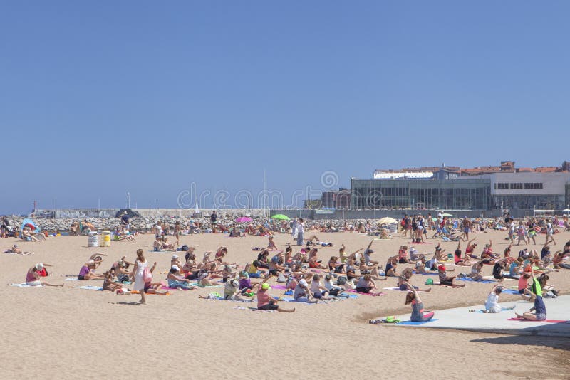 Gijon beach, Asturias, Spain, July 10, 2019: Joyous women exercising yoga poses on sunny beach. Gijon beach, Asturias, Spain, July 10, 2019: Joyous women exercising yoga poses on sunny beach