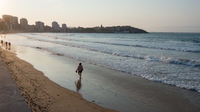 Gijon beach and seafront at sunset. Woman walking alone on the seashore. Waves on the sea. Asturias, Spain, Europe