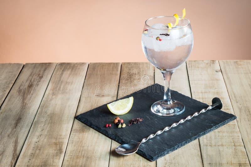 Gin Tonic with botanicals and bar spoon on wood table.