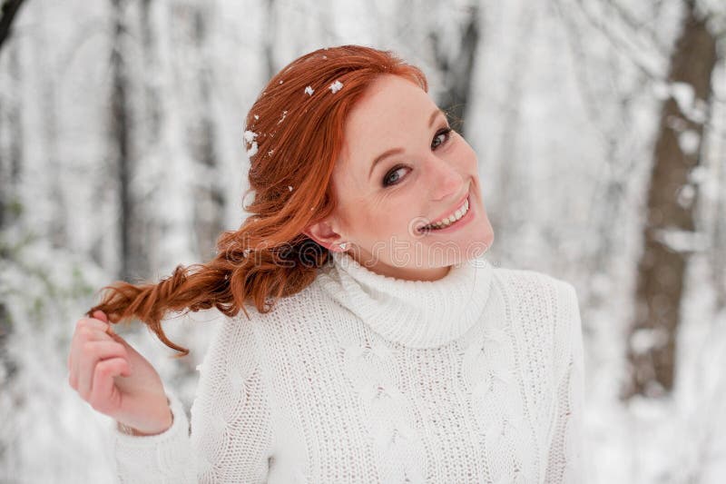 Ginger pretty girl in white sweater in winter forest. Snow december in park. Portrait. Christmas cute time.