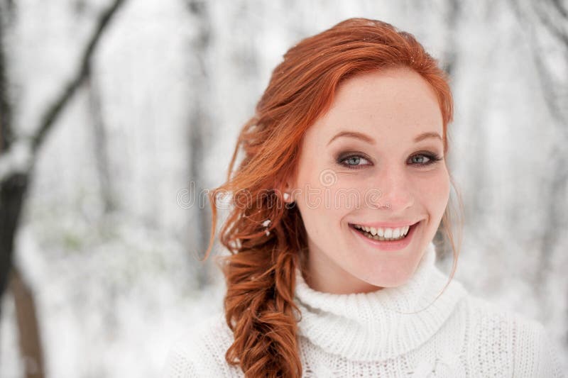 Ginger smiling girl in white sweater in winter forest. Snow december in park. Portrait. Christmas cute time.