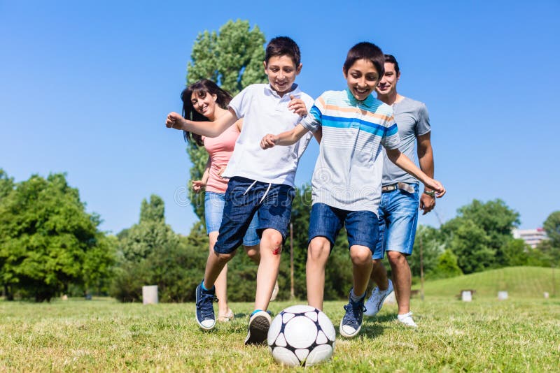 Giocar a calcioe o calcio della famiglia in parco di estate fotografia stock Giocar a calcioe o calcio della famiglia in parco di estate fotografia stock