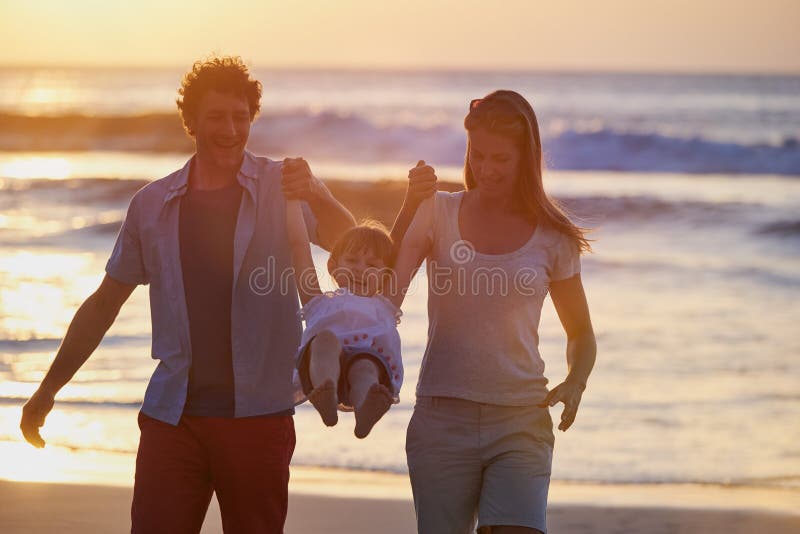 Giocare con una ragazza e i genitori che si tengono per mano in spiaggia per divertimento durante le vacanze e si legano all'avven fotografia stock